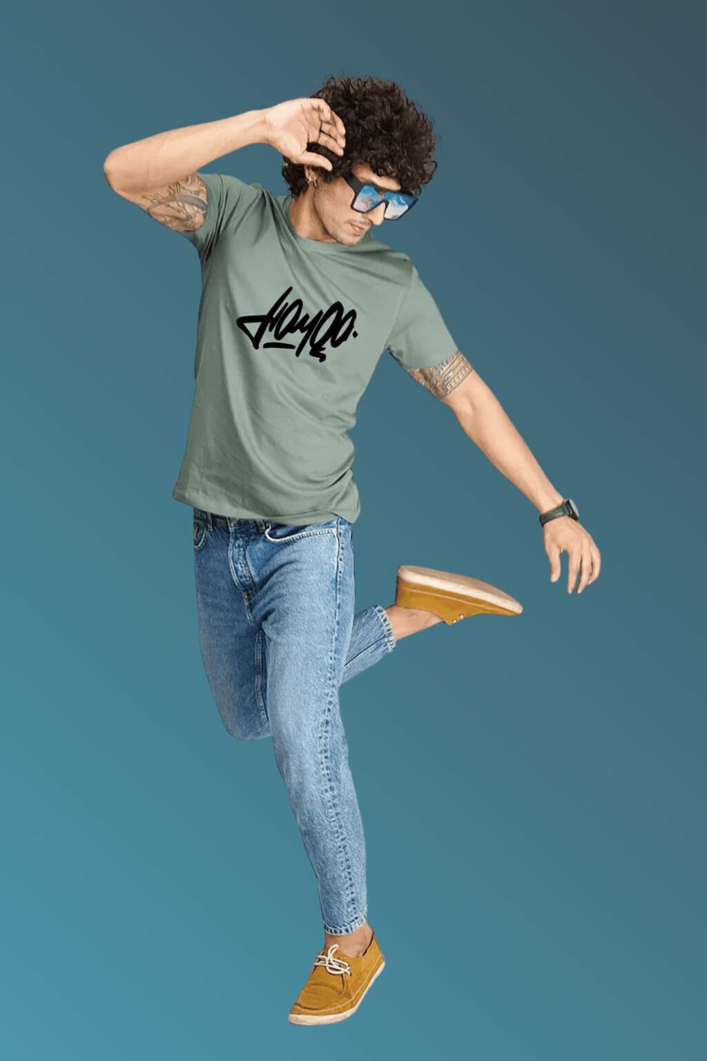 t-shirt featuring bold black stylized typography, worn with blue denim jeans and brown casual shoes. Set against a smooth blue gradient backdrop, the photo highlights modern streetwear style in a minimal, fashion-forward composition."
