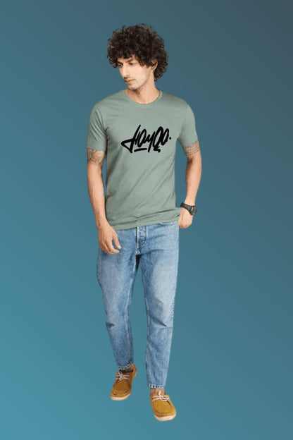 t-shirt featuring bold black stylized typography, worn with blue denim jeans and brown casual shoes. Set against a smooth blue gradient backdrop, the photo highlights modern streetwear style in a minimal, fashion-forward composition."