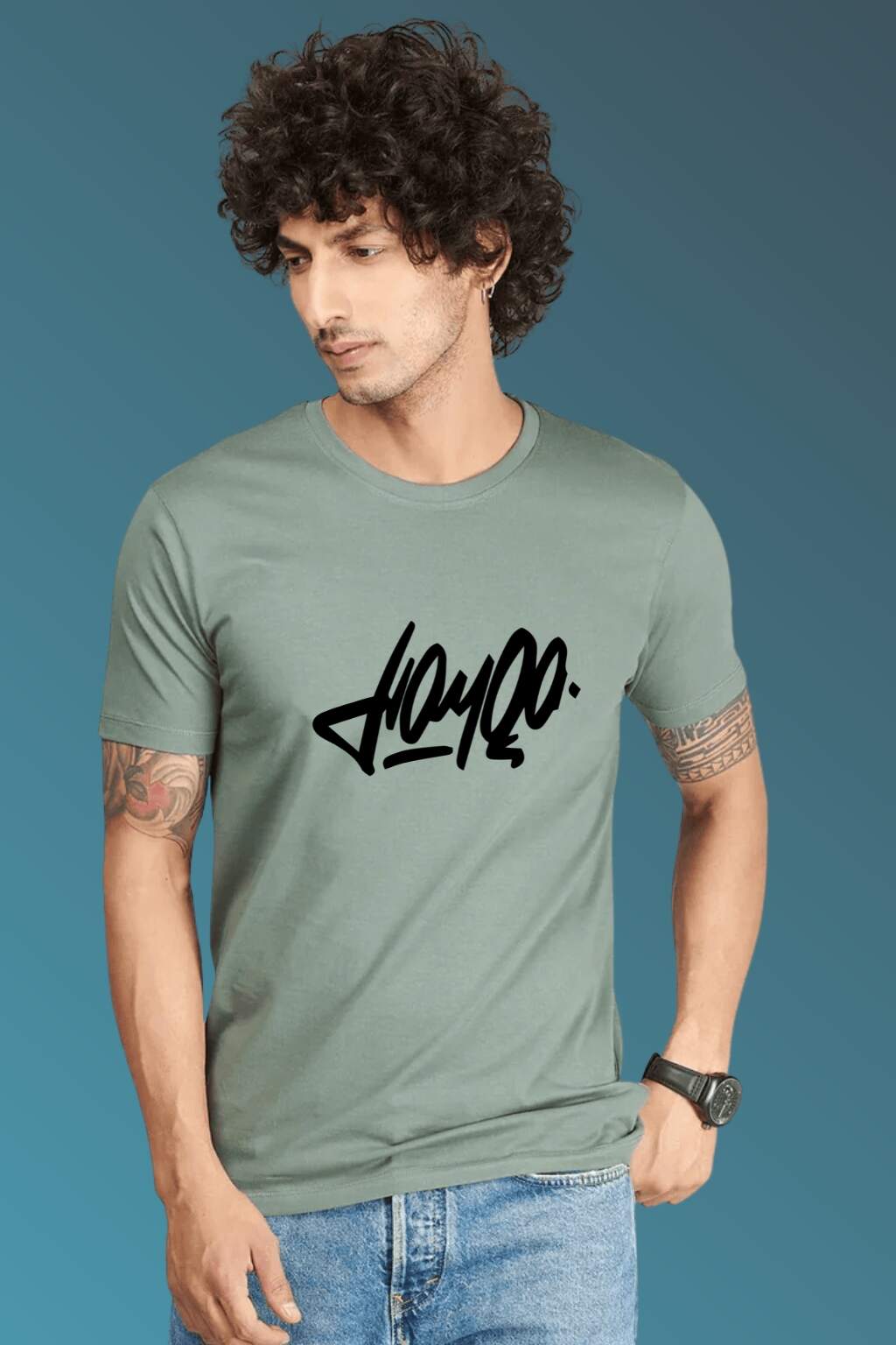 t-shirt featuring bold black stylized typography, worn with blue denim jeans and brown casual shoes. Set against a smooth blue gradient backdrop, the photo highlights modern streetwear style in a minimal, fashion-forward composition."